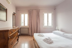 A hotel room with a wooden dresser, a bed with white linens, and two windows with curtains.