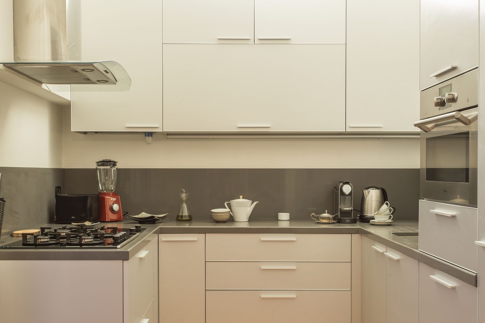 A modern kitchen with white cabinets, a gas stove, a blender, a coffee maker, and a microwave.