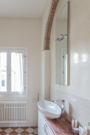 A bathroom with a white sink, a large mirror, a window with curtains, and a radiator.