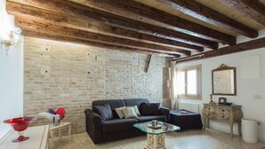 Ein Wohnzimmer mit Steinwand, einem dunklen Sofa, einem Glastisch und einem kleinen Beistelltisch.