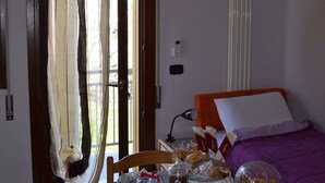 A breakfast table set with various food items, a bed with a purple blanket, and a window with curtains. - B&B Ca' Gialla (Urbana)
