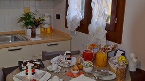 A dining table set with various dishes, a window with curtains, and a kitchen area with cabinets and a sink. - B&B Ca' Gialla (Urbana)