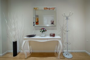 Une console blanche ornée d’un vase de fleurs, d’une petite boîte rouge et d’une assiette noire. Une grande lampe sur pied blanche se trouve à côté de la console.