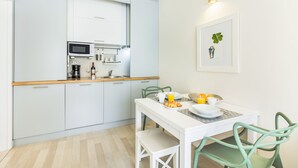 Eine moderne Küche mit weißen Schränken, einer Mikrowelle und einer Kaffeemaschine. Ein Esstisch mit Stühlen und ein gerahmtes Bild an der Wand sind ebenfalls vorhanden.