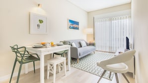 Ein modernes Wohnzimmer mit einer Couch, einem Esstisch mit Stühlen und einem großen Fenster mit Jalousien.