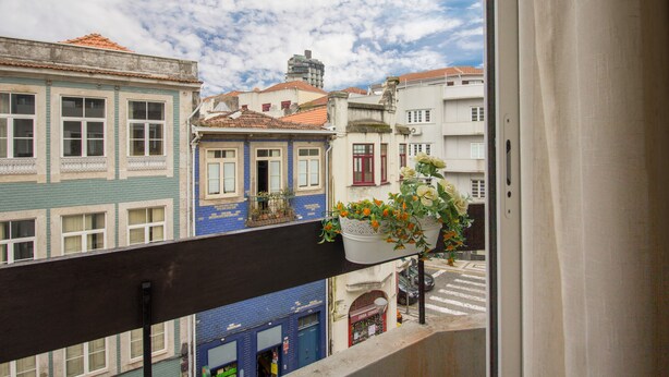 Ein Balkon mit Blick auf eine Straße und Gebäude, darunter ein blaues Gebäude mit weißer Fassade und ein weißes Gebäude mit roter Tür.