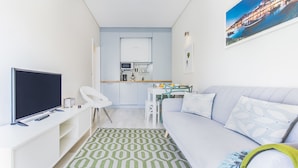 Ein kompakter Wohnbereich mit Sofa, Fernseher, kleiner Küchenzeile und Esstisch.