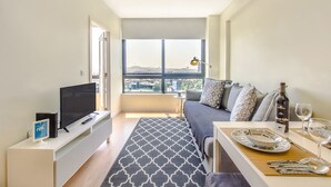 A modern living room with a large window, a flat-screen TV, a sofa, a dining table set with plates and glasses, and a bottle of wine. - Trindade Flat with Great View (Porto)