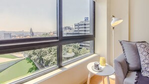 A room with a large window offering a city view, a modern lamp, a small table with a cup, and a patterned throw on a sofa. - Trindade Flat with Great View (Porto)