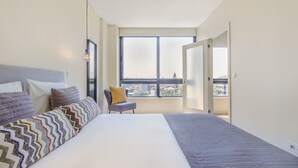 A modern bedroom with a large bed, a chair, and a view of the city through a large window. - Trindade Flat with Great View (Porto)
