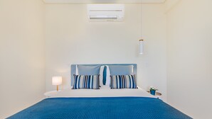 Un letto ben rifatto con una coperta a quadri blu, due cuscini a righe, una lampada da comodino e una piccola pianta in vaso.