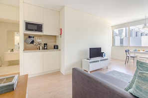 A compact living space with a kitchenette, a flat-screen TV, a sofa, and a dining area with a table and chairs. - Trindade Modern Flat (Porto)