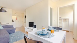 Un soggiorno moderno con un divano, un tavolo da pranzo apparecchiato con piatti e bicchieri azzurri e una TV su un mobile bianco.