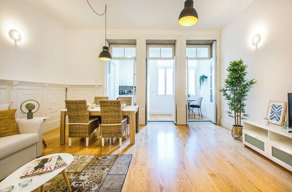 A modern living room with a dining area, wooden flooring, and a large window. - Santa Catarina Downtown Flat (Porto)