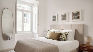 A bedroom with a bed, a bedside table with a lamp, a window, and three framed artworks on the wall. - São Mamede Downtown Apartment (Lisbon)