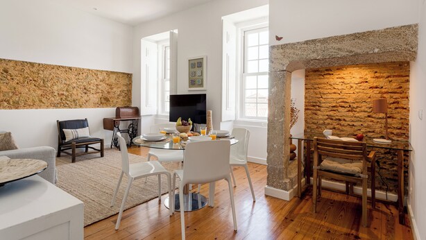 A modern living room with a stone wall, a fireplace, and a dining area with a round table and chairs. - São Mamede Downtown Apartment (Lisbon)