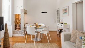 A modern living room with a dining area, featuring a glass table, white chairs, a sofa, and a fireplace. - São Mamede Downtown Apartment (Lisbon)