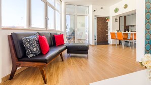 A modern living room with a leather sofa, a dining area with orange chairs, and a kitchen in the background.