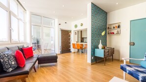 A modern living room with a sofa, a dining area, and a kitchen in the background.