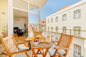Ein Balkon mit Holzstühlen und einem Tisch, gedeckt mit Frühstücksgebäck, mit Blick auf eine Stadtlandschaft.