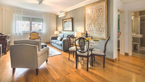 Een woonkamer met een eethoek, een bank, stoelen en een tafel met een bloevas.