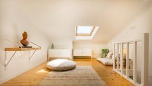 A spacious attic room with a skylight, wooden flooring, a white sofa, a patterned rug, and a small Buddha statue. - Amazing Castle Views in Historic Center (Lisbon)