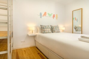 A bedroom with a bed, two bedside tables with lamps, a wall-mounted artwork of birds, and a mirror. - Amazing Castle Views in Historic Center (Lisbon)