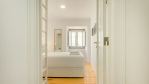 A narrow hallway leading to a bedroom with a bed, a window, and a mirror. - Amazing Castle Views in Historic Center (Lisbon)