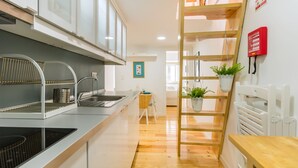 A modern kitchen with a stainless steel sink, wooden flooring, and a built-in stove. There is a wooden ladder leading to a loft area with a plant. - Amazing Castle Views in Historic Center (Lisbon)