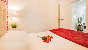 A hotel room with a bed, a red blanket, a bouquet of flowers, a lamp, and a small plant on the nightstand. - Steps Lisbon @ Historical Center (Lisbon)