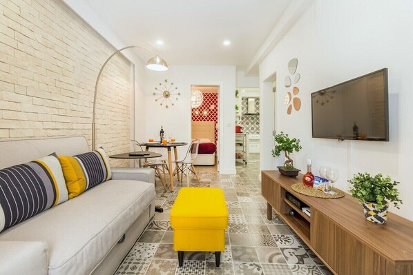 A modern living room with a sofa, ottoman, TV, and a dining area with chairs and a table. - Steps Lisbon @ Historical Center (Lisbon)