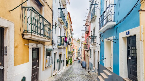 A narrow cobblestone street lined with colorful buildings, each with balconies and doors. - Steps Lisbon @ Historical Center (Lisbon)