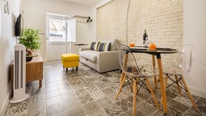 A modern living room with a sofa, a dining table with chairs, a small yellow ottoman, a potted plant, and a TV mounted on the wall. - Steps Lisbon @ Historical Center (Lisbon)