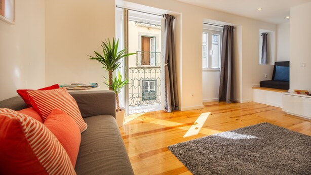 A modern living room with a grey sofa, red cushions, a potted plant, and a wooden floor. - Bica Historical Tram Apartment (Lisbon)