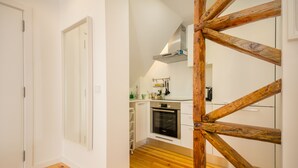 A modern kitchen with white cabinets, a wooden floor, and a built-in oven. - Bica Historical Tram Apartment (Lisbon)