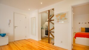 A spacious room with wooden flooring, a bed with a red blanket, a kitchen area, and a staircase leading to another level. - Bica Historical Tram Apartment (Lisbon)