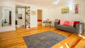 A modern living room with a grey sofa, wooden flooring, a dining area with a table and chairs, and a kitchen in the background. - Bica Historical Tram Apartment (Lisbon)
