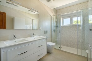 Un baño moderno con un tocador doble, un inodoro y cabina de ducha con paredes de cristal.