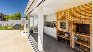 A modern kitchen with a brick oven, white cabinets, and a glass door leading to a patio area with a pool. - Casa de Monsanto I Lamego (Lamego)
