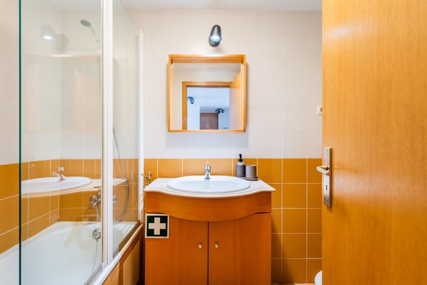 A bathroom with a bathtub, two sinks, a mirror, and a wooden cabinet. - Olaias Flat (Lisbon)