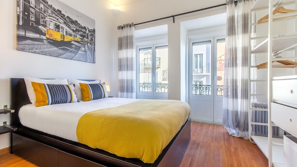 A modern hotel room with a large bed, a wardrobe, a balcony with a view, and a painting on the wall. - Paraíso Alfama (Lisbon)