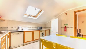 A kitchen with a skylight, a dishwasher, a microwave, and a table with yellow chairs. - Casa Mouraria I Castle Views (Lisbon)