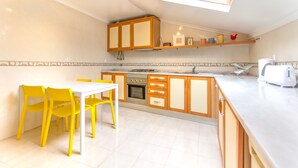 A modern kitchen with a skylight, a dining area with yellow chairs, and wooden cabinets. - Casa Mouraria I Castle Views (Lisbon)