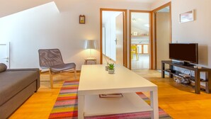 A modern living room with a sofa, a chair, a coffee table, a TV stand, and a colorful rug. - Casa Mouraria I Castle Views (Lisbon)