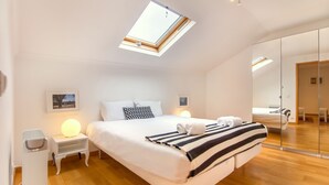 A modern bedroom with a skylight, a large bed with striped bedding, bedside lamps, and a wooden floor. - Casa Mouraria I Castle Views (Lisbon)