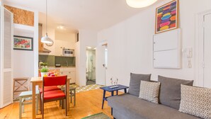 A modern living room with a grey sofa, red chair, wooden dining table, and a small blue side table. - São Vicente Heart of Alfama (Lisbon)