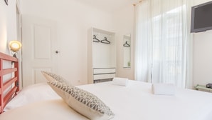 A hotel room with a bed, a wardrobe, a mirror, a TV, and a window with curtains. - São Vicente Heart of Alfama (Lisbon)