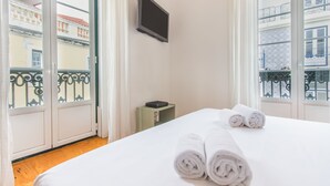 A hotel room with a bed, a flat-screen TV, and a view of buildings through the windows. - São Vicente Heart of Alfama (Lisbon)