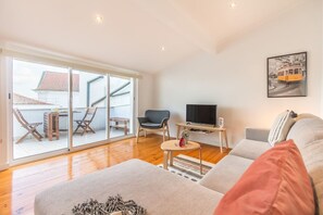 Ein modernes Wohnzimmer mit einer Couch, einem Fernseher und einem Balkon mit Stühlen und einem Tisch.