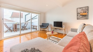 Una sala moderna con un sofá, televisión y un comedor con sillas y una mesa.